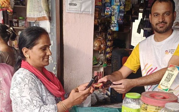 A woman completing a digital payment at a village shop counter, Vikasnagar